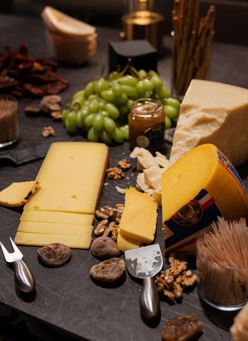 Verschiedene Käsesorten, Weintrauben, Feigen, Walnüsse und Grissini sind auf einer dunklen Schieferplatte arrangiert. Käsemesser und ein kleines Glas Senf sind ebenfalls vorhanden. | casaceramica