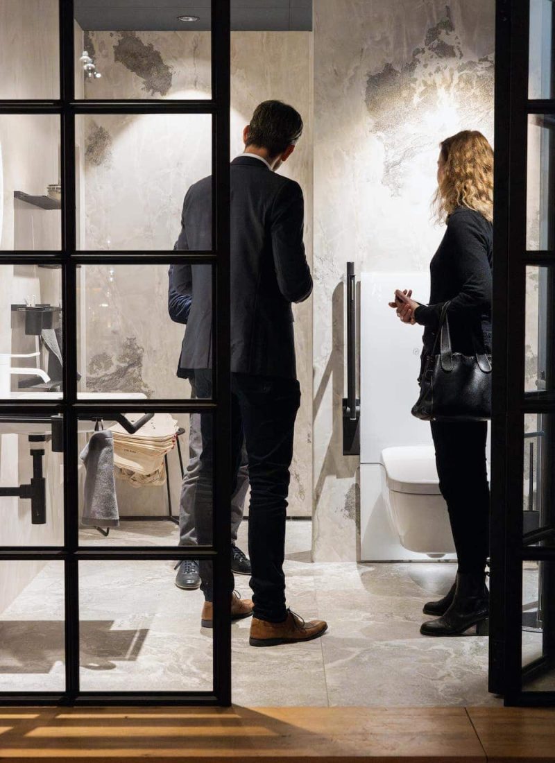 Zwei Menschen stehen in einem modernen Badezimmer mit Glaswänden und unterhalten sich. | casaceramica
