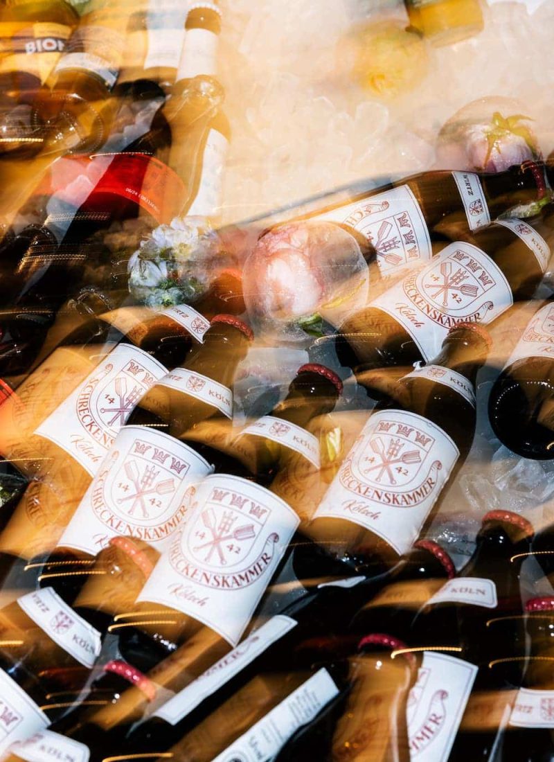 Eine Auswahl an Bieren mit weißen Etiketten mit rotem Text und Emblem ist zusammen mit Eis und anderen Getränken aufgestapelt. | casaceramica