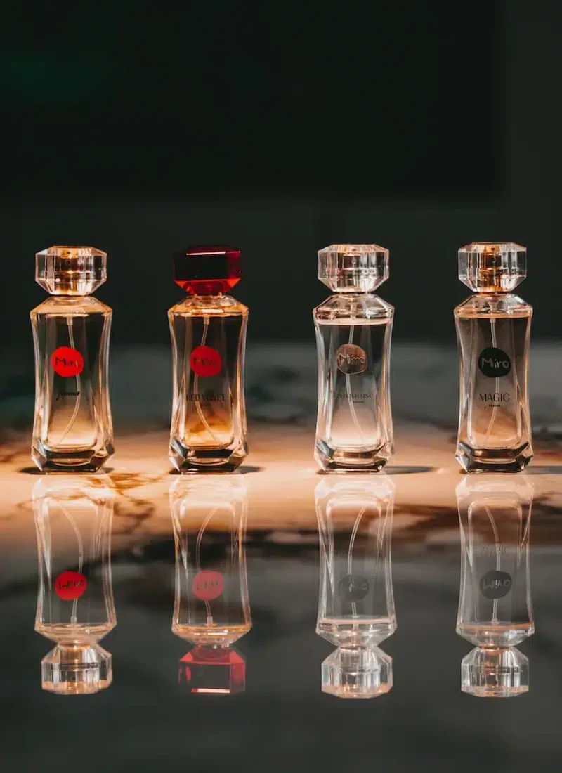 Convary Vier Parfümflaschen aus Glas mit verschiedenfarbigen Verschlüssen und Etiketten, präsentiert auf einer reflektierenden Oberfläche. | casaceramica