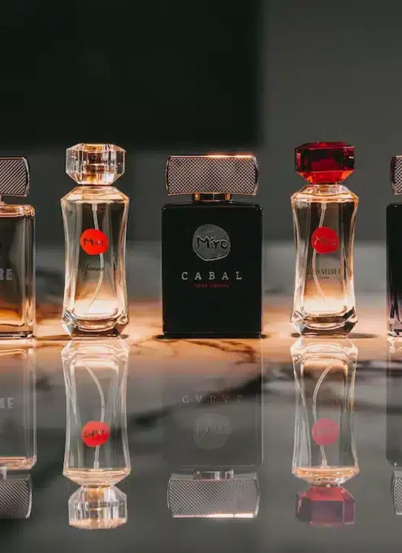 Sechs Parfümflakons in verschiedenen Farben und mit unterschiedlichen Etiketten sind auf einer reflektierenden Oberfläche aufgereiht. Jeder Flakon ist rechteckig und hat einen facettierten Verschluss. | casaceramica