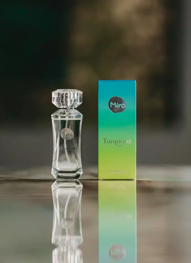 Convary Eine Flasche Miro Turquoise-Parfüm neben ihrer türkis-grünen Schachtel, auf einer reflektierenden Oberfläche platziert. | casaceramica