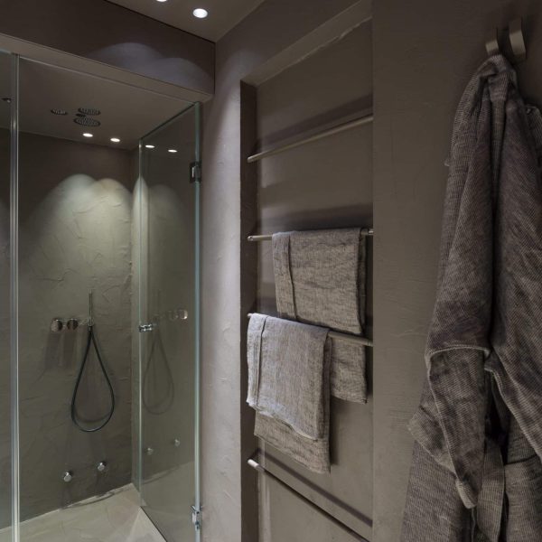 Grau gespachteltes Badezimmer mit inklusiver Dampfsauna und Infrarot Heizung. Neben der Heizung hängt ein Bademantel von Luiz.